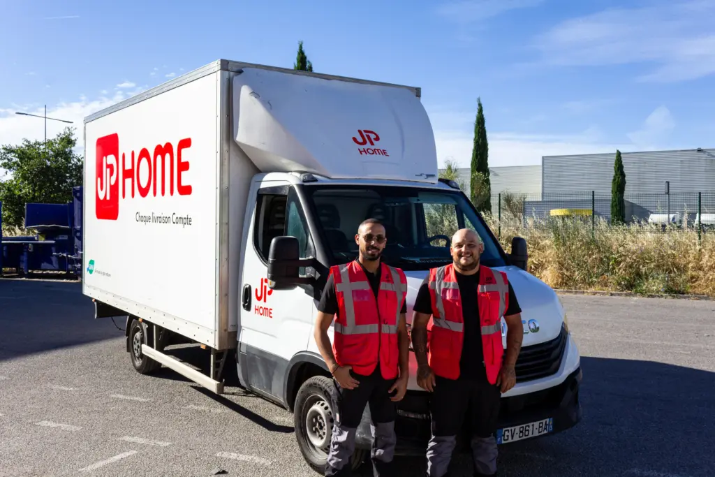 Deux livreurs en gilet rouge posent devant un camion de livraison JP Home