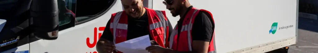 Deux hommes en gilets de sécurité examinent un document devant un camion blanc