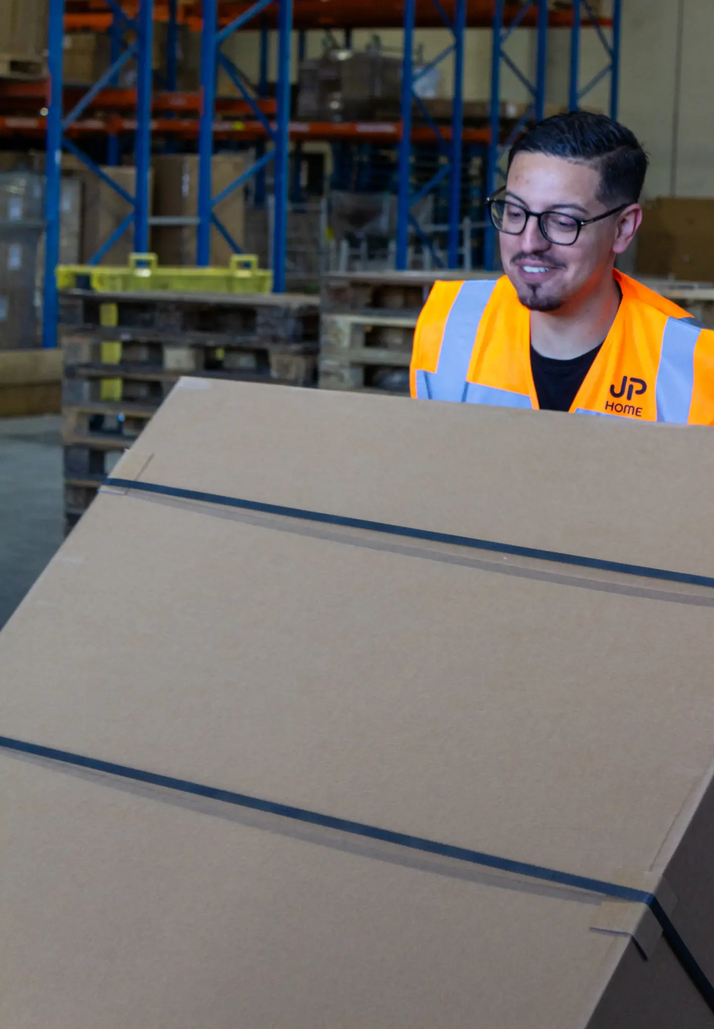 Collaborateur JP HOME manipulant un colis dans un entrepôt logistique avant expédition.