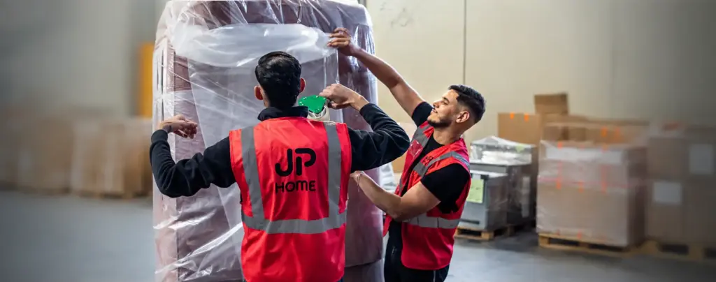 Deux manutentionnaires emballent un meuble sous film plastique dans un entrepôt